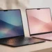 Two laptops side by side on a desk — one dark aluminum, one blush pink — representing the Googlebook and MacBook Neo comparison