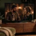 A modern flat-screen TV in a dim living room showing a cinematic period-drama scene.
