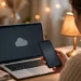 Woman at a home desk checking her smartphone while her laptop shows a disconnected cloud icon, illustrating how to check whether a website is down