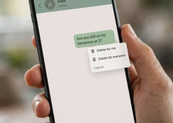 A hand holding a smartphone showing a messaging chat with a message bubble and a pop-up menu offering "Delete for me" and "Delete for everyone"